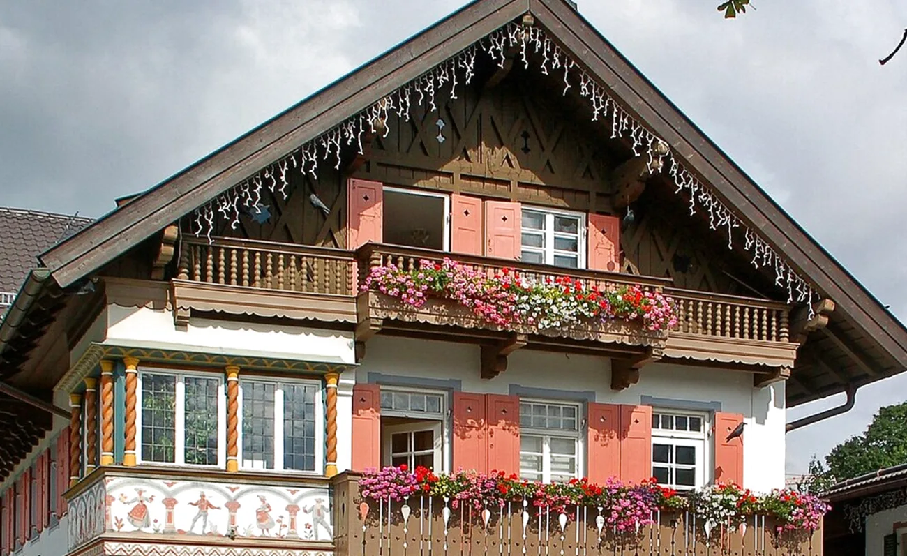 Bemalte Fassade eines alten Dorfhauses mit geschnitztem Balkon und Blumenkästen